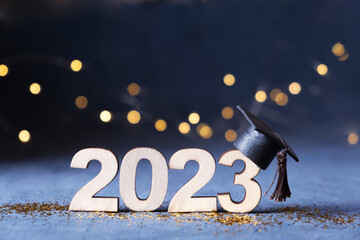 Class of 2023 concept. Wooden number 2023 with graduate hat on dark background with bokeh