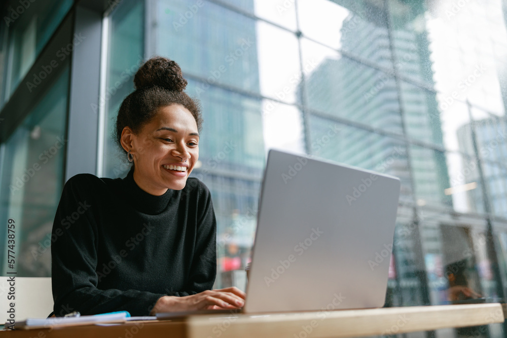 Smiling female freelancer working on laptop while sitting in cafe near window. Distance work 