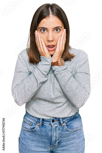 Young beautiful woman wearing casual turtleneck sweater afraid and shocked, surprise and amazed expression with hands on face