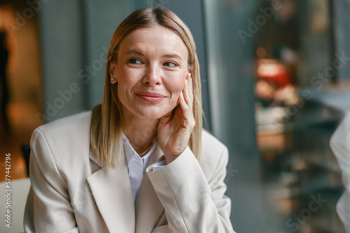 Close up portrait of attractive smiling businesswoman in jacket sitting in cafe and looking at side