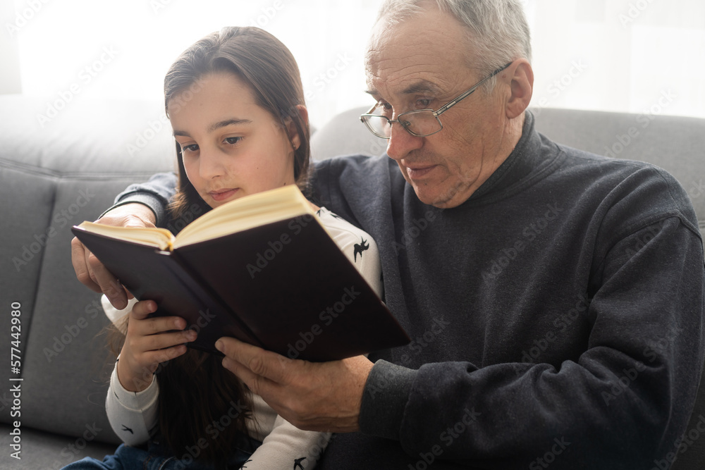 Book, family and children with a girl reading to her grandfather on the floor of their living at home. Kids, read and story with a senior man and granddaughter bonding in their house during a visit. Book, family and children with a girl reading to her grandfather on the floor of their living at home. Kids, read and story with a senior man and granddaughter bonding in their house during a visit.