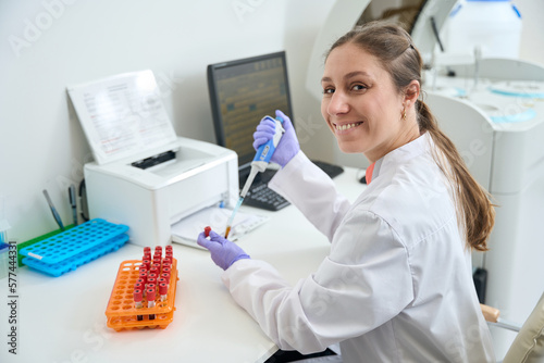 Smiling laboratory employee at her workplace works with blood samples photo