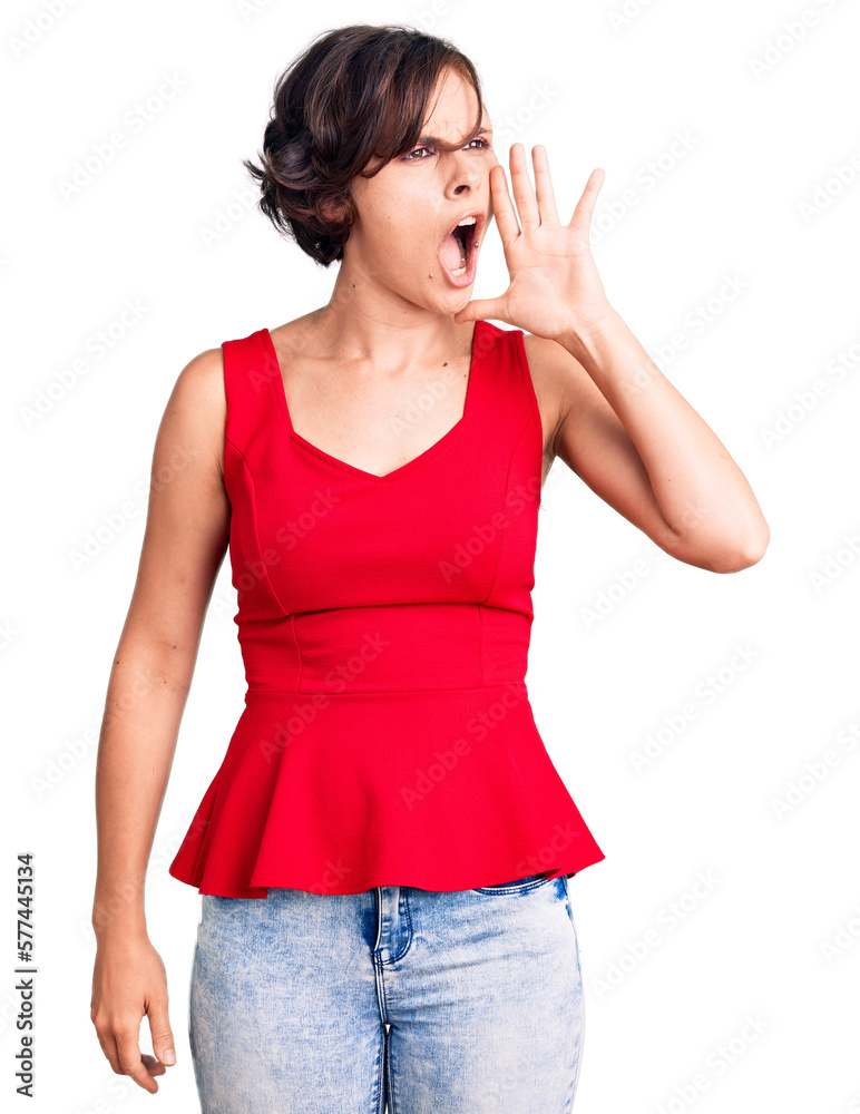 Beautiful young woman with short hair wearing casual style with sleeveless shirt shouting and screaming loud to side with hand on mouth. communication concept. Beautiful young woman with short hair wearing casual style with sleeveless shirt shouting and screaming loud to side with hand on mouth. communication concept.