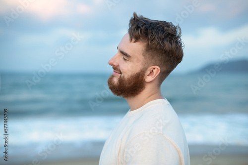 Portrait of happy young bearded guy, handsome man on the sea or ocean walking on beach enjoying good summer weather at vacation in tropical country