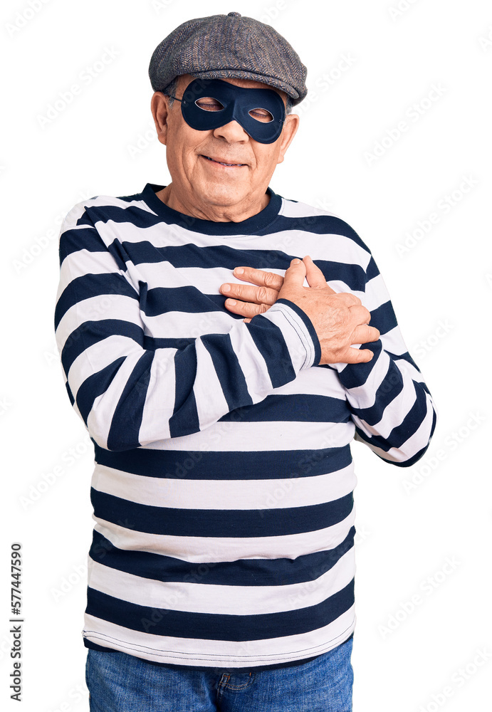Senior handsome man wearing burglar mask and t-shirt smiling with hands on chest with closed eyes and grateful gesture on face. health concept.