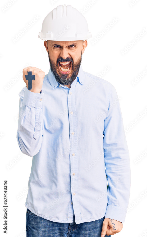 Young handsome man wearing architect hardhat angry and mad raising fist frustrated and furious while shouting with anger. rage and aggressive concept. Young handsome man wearing architect hardhat angry and mad raising fist frustrated and furious while shouting with anger. rage and aggressive concept.
