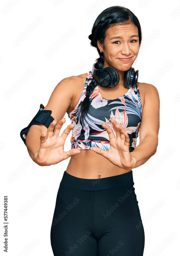 Beautiful hispanic woman wearing sportswear and headphones disgusted expression, displeased and fearful doing disgust face because aversion reaction. with hands raised Beautiful hispanic woman wearing sportswear and headphones disgusted expression, displeased and fearful doing disgust face because aversion reaction. with hands raised