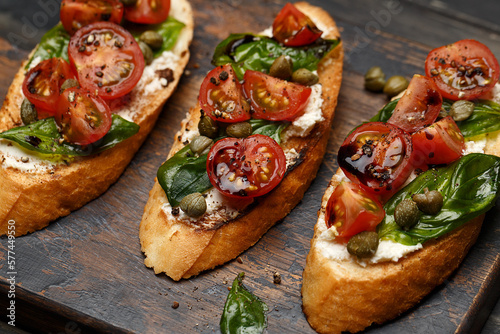 Photos Traditional italian bruschetta with cherry tomatoes, cream cheese, basil leaves, capers and balsamic vinegar on wooden cutting board