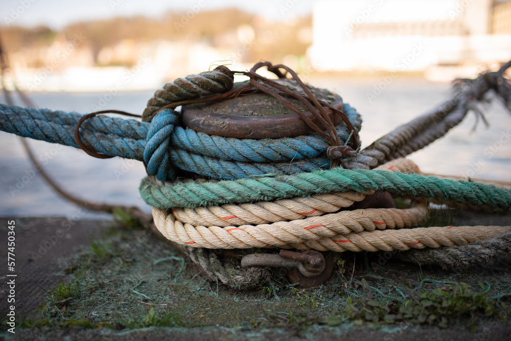 A mooring bollard entwined with a mooring rope. Moored ships at the port quay. Season winter.