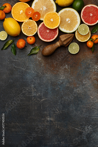 Set of various fresh citrus fruits with leaves and wooden juicer on dark concrete background. Healthy food backround. Flat composition with copy space. Overhead view © Zygonema