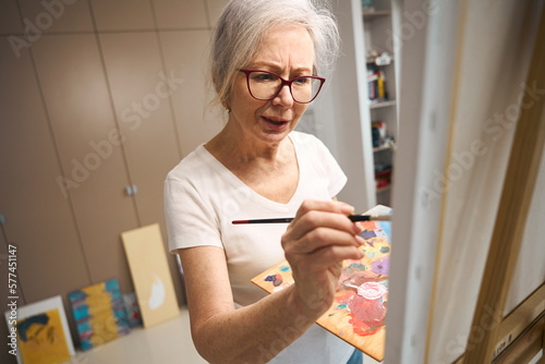 Talented elderly lady paints a picture in a bright room