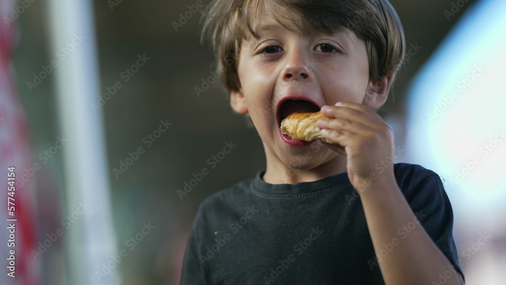 One cute small boy eating piece of bread outside. Child eats snack One cute small boy eating piece of bread outside. Child eats snack