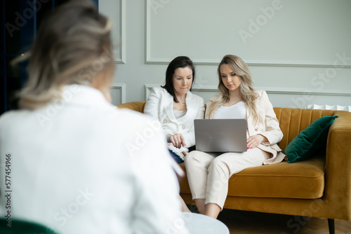Group of businesswomen is working on project, two are sitting on couch in office, one of them is pregnant with laptop. 
