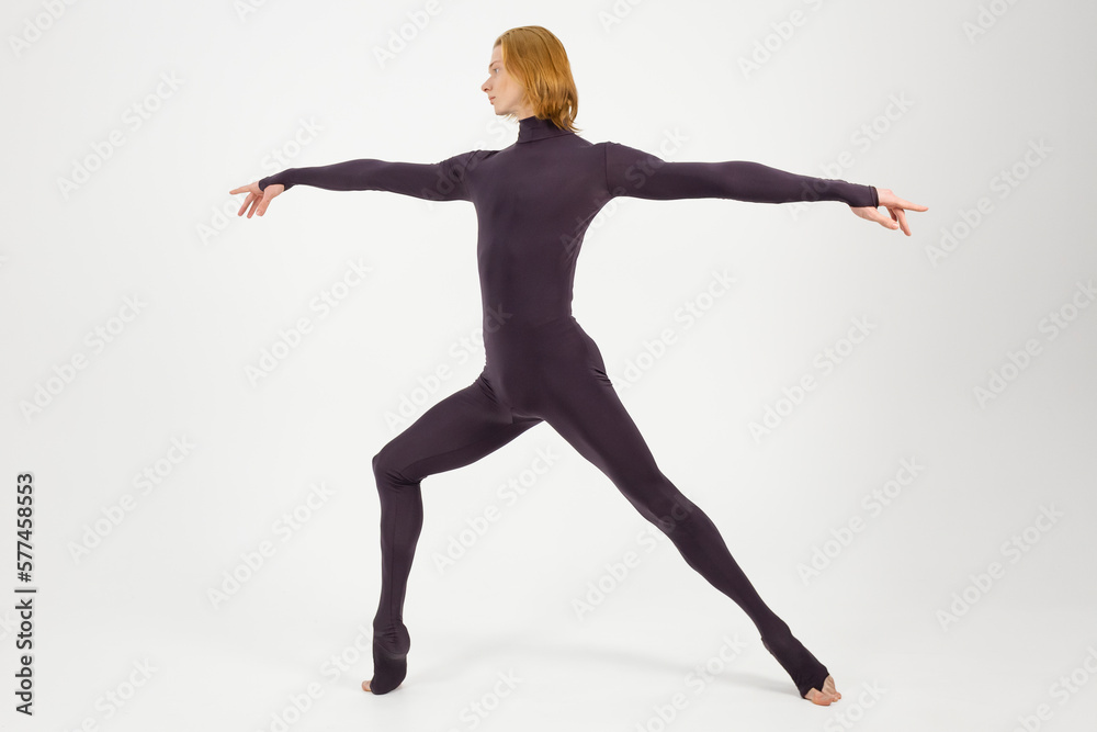 Young athletic professional ballet dancer in a black unitard is in perfect shape and performing over a white background.