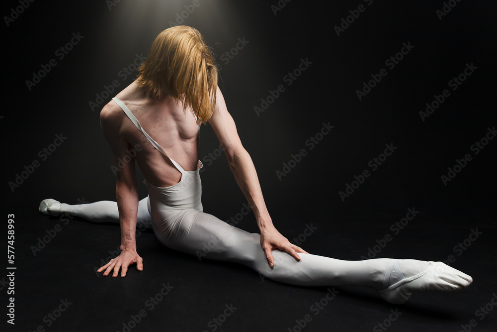 Young athletic professional ballet dancer with a bare torso and white dance tights is in perfect shape, performing and doing splits over a black background. Young athletic professional ballet dancer with a bare torso and white dance tights is in perfect shape, performing and doing splits over a black background.