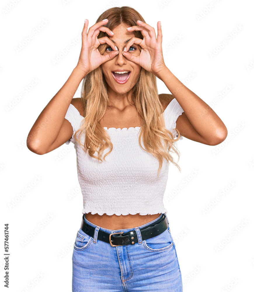 Beautiful blonde young woman wearing casual white tshirt doing ok gesture like binoculars sticking tongue out, eyes looking through fingers. crazy expression.