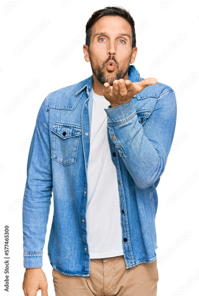Young handsome man wearing casual denim jacket looking at the camera blowing a kiss with hand on air being lovely and sexy. love expression. Young handsome man wearing casual denim jacket looking at the camera blowing a kiss with hand on air being lovely and sexy. love expression.