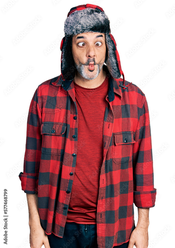Middle age hispanic man with grey hair wearing fluffy earmuff hat making fish face with lips, crazy and comical gesture. funny expression. Middle age hispanic man with grey hair wearing fluffy earmuff hat making fish face with lips, crazy and comical gesture. funny expression.