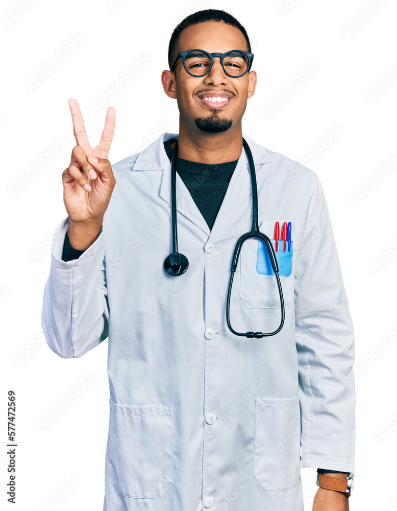 Young african american man wearing doctor uniform and stethoscope smiling looking to the camera showing fingers doing victory sign. number two. Young african american man wearing doctor uniform and stethoscope smiling looking to the camera showing fingers doing victory sign. number two.