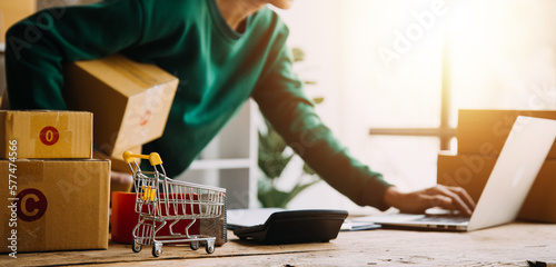 Startup SME small business entrepreneur of freelance Asian woman wearing apron using laptop and box to receive and review orders online to prepare to pack sell to customers, online sme business ideas.