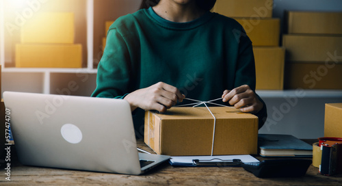 Startup SME small business entrepreneur of freelance Asian woman wearing apron using laptop and box to receive and review orders online to prepare to pack sell to customers, online sme business ideas.