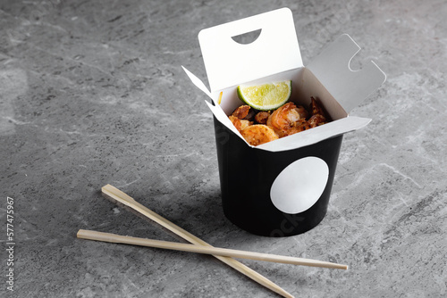 Chinese food in a black takeout box on a gray background. Sushi chopsticks and a black box.