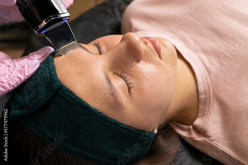 Doctor dermatologist with ultrasonic scraber doing procedure of ultrasonic cleaning of female, teenage girl face in healthcare clinic, spa salon. Facial peeling, beauty treatment.Cosmetology. Closeup. photo
