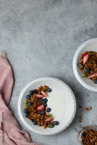 Nut granola bowl with yogurt, blueberry and strawberry. Healthy breakfast with oat crunchy muesli. Pink textile napkin, glass jar. Grey background. Top view. Copy space