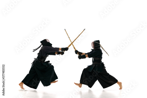 Dynamic image of two men, professional kendo athletes training with bamboo shinai sword against white studio background. Concept of martial arts, sport, Japanese culture, action and motion