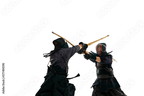 Two men, professional kendo athletes in special uniform training, fighting with shinai sword against white studio background. Concept of martial arts, sport, Japanese culture, action and motion