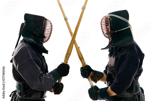Two men, professional kendo fighter, athletes in black uniform training, crossing swords against white studio background. Concept of martial arts, sport, Japanese culture, action and motion