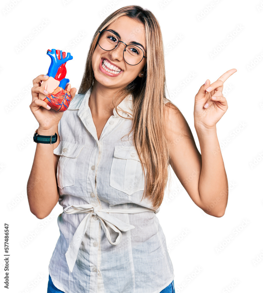 Obraz premium Hispanic young woman holding heart organ smiling happy pointing with hand and finger to the side
