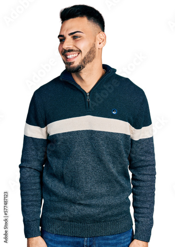 Young hispanic man with beard wearing casual winter sweater looking away to side with smile on face, natural expression. laughing confident.