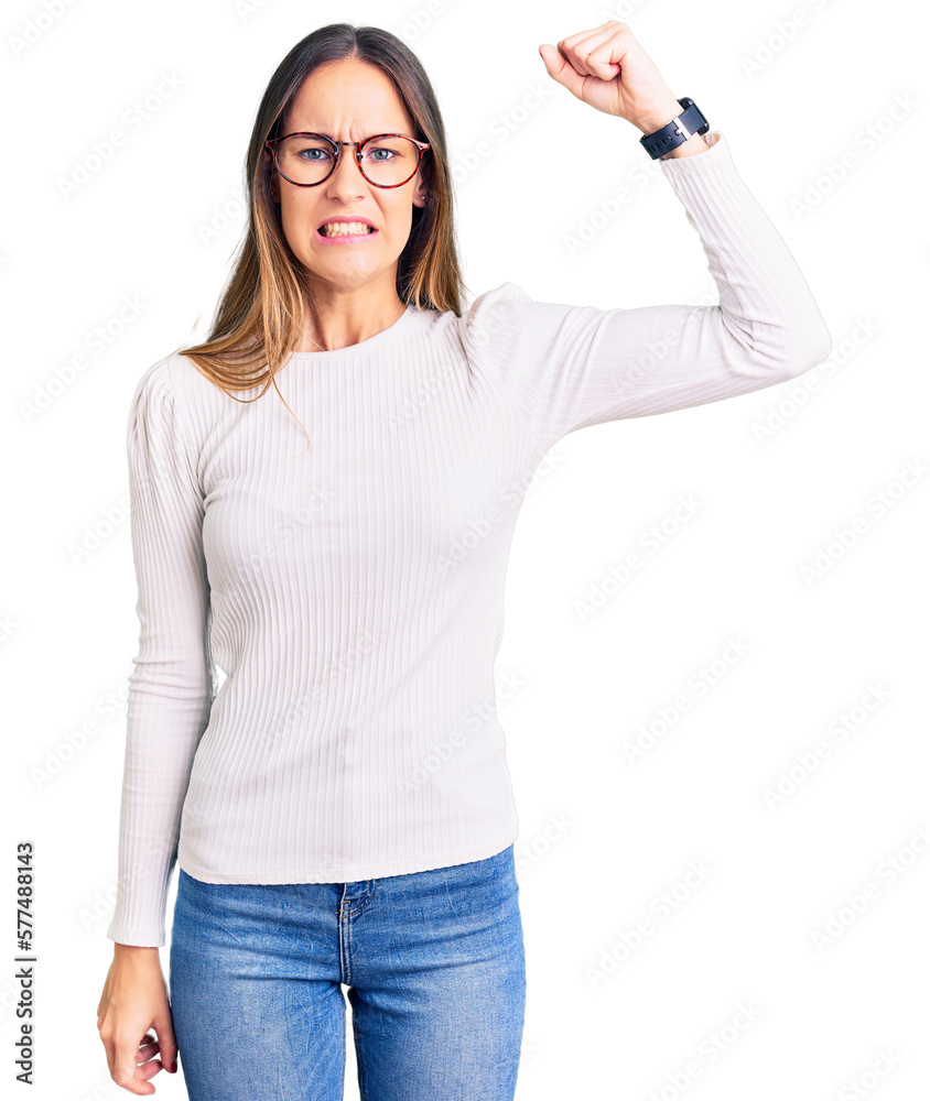 Beautiful brunette young woman wearing casual white sweater and glasses angry and mad raising fist frustrated and furious while shouting with anger. rage and aggressive concept. Beautiful brunette young woman wearing casual white sweater and glasses angry and mad raising fist frustrated and furious while shouting with anger. rage and aggressive concept.