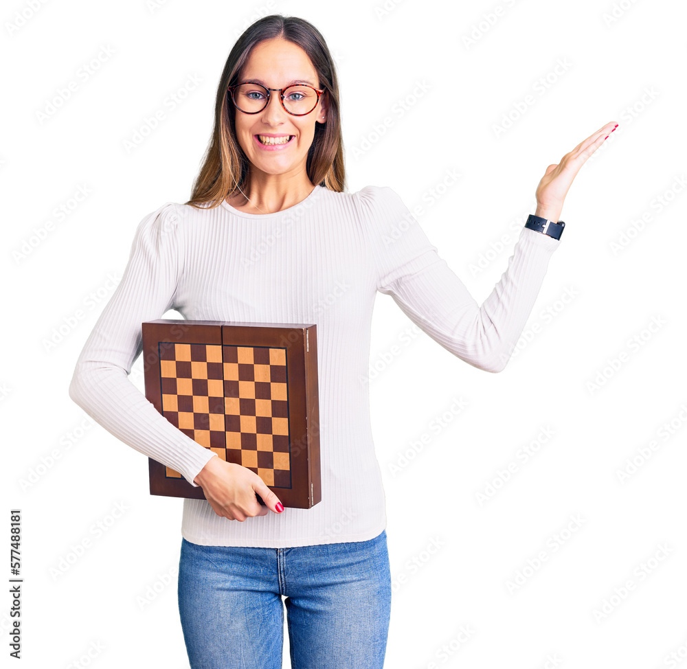Beautiful brunette young woman holding chess celebrating victory with happy smile and winner expression with raised hands