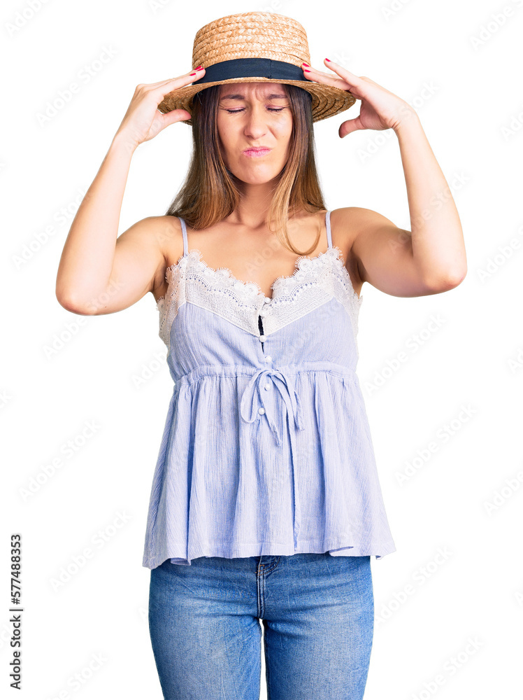 Beautiful brunette young woman wearing summer hat suffering from headache desperate and stressed because pain and migraine. hands on head. Beautiful brunette young woman wearing summer hat suffering from headache desperate and stressed because pain and migraine. hands on head.