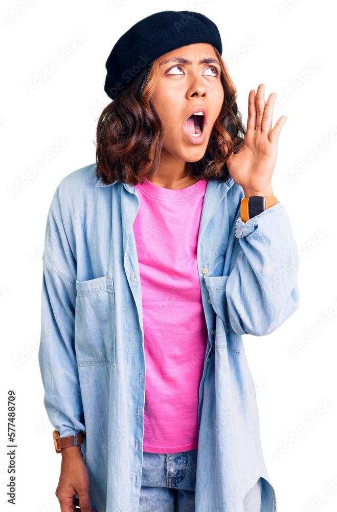 Young beautiful mixed race woman wearing french look with beret shouting and screaming loud to side with hand on mouth. communication concept. Young beautiful mixed race woman wearing french look with beret shouting and screaming loud to side with hand on mouth. communication concept.