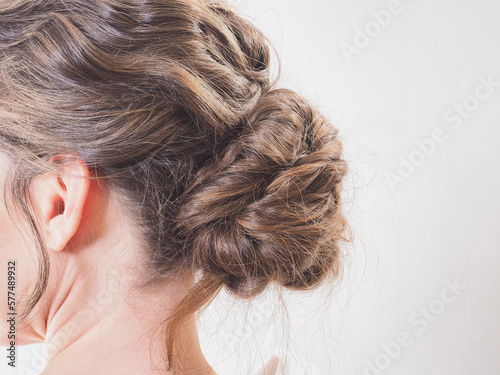  A beautiful girl gathered her wavy hair in a low bundle. Modern festive hairstyle for long brown hair. A woman braided a bunch or bun on her head on a white background. Back and side view close up
