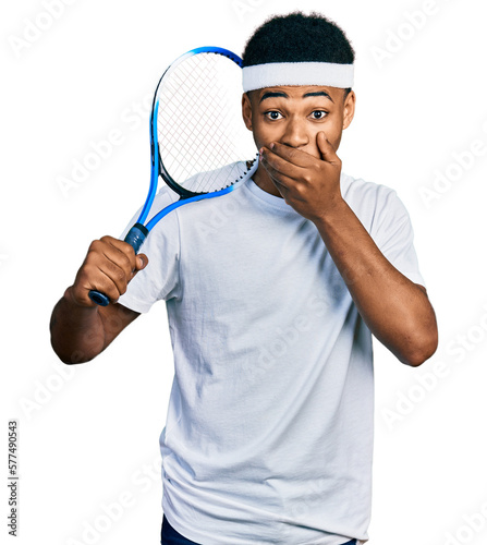 Young african american man playing tennis holding racket covering mouth with hand, shocked and afraid for mistake. surprised expression