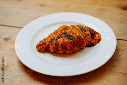 Close up shot of a fresh croissant with poppy seeds laying on a white plate.