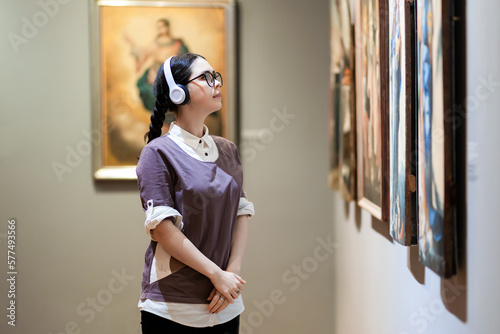 Fotografia Side view of young Caucasian pretty woman wearing headphones and contemplates ancient artefacts