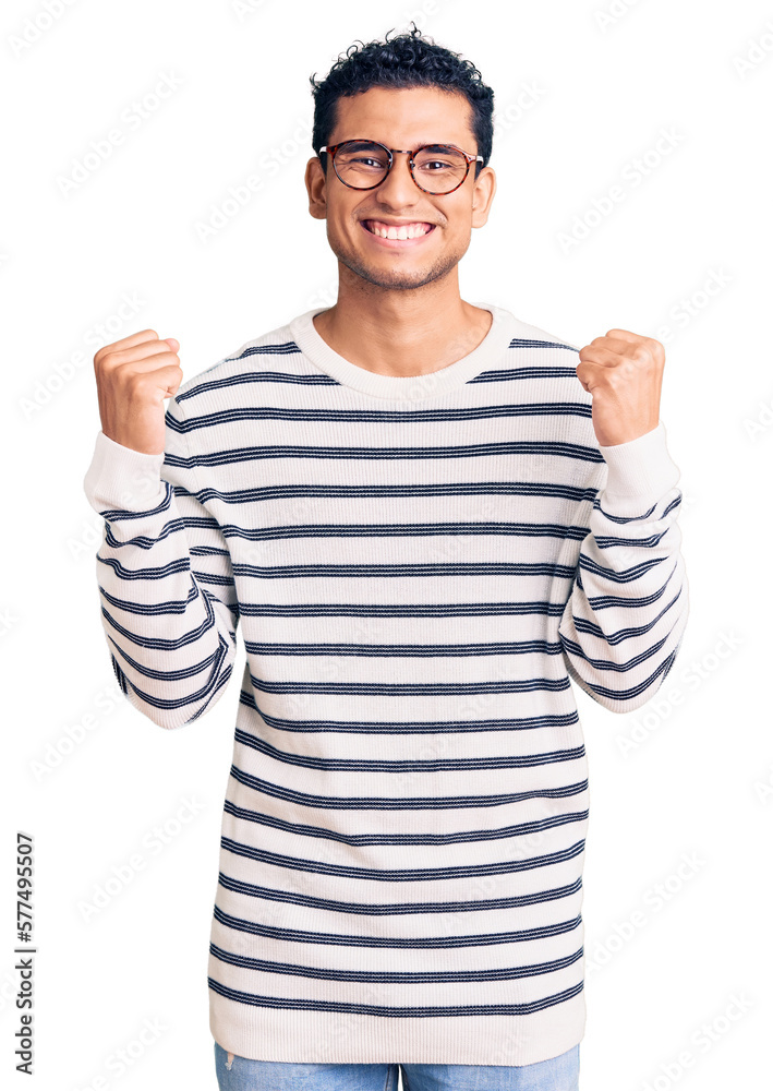 Hispanic handsome young man wearing casual clothes and glasses celebrating surprised and amazed for success with arms raised and open eyes. winner concept. Hispanic handsome young man wearing casual clothes and glasses celebrating surprised and amazed for success with arms raised and open eyes. winner concept.
