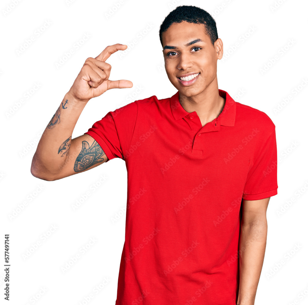 Young hispanic man wearing casual red t shirt smiling and confident gesturing with hand doing small size sign with fingers looking and the camera. measure concept. Young hispanic man wearing casual red t shirt smiling and confident gesturing with hand doing small size sign with fingers looking and the camera. measure concept.