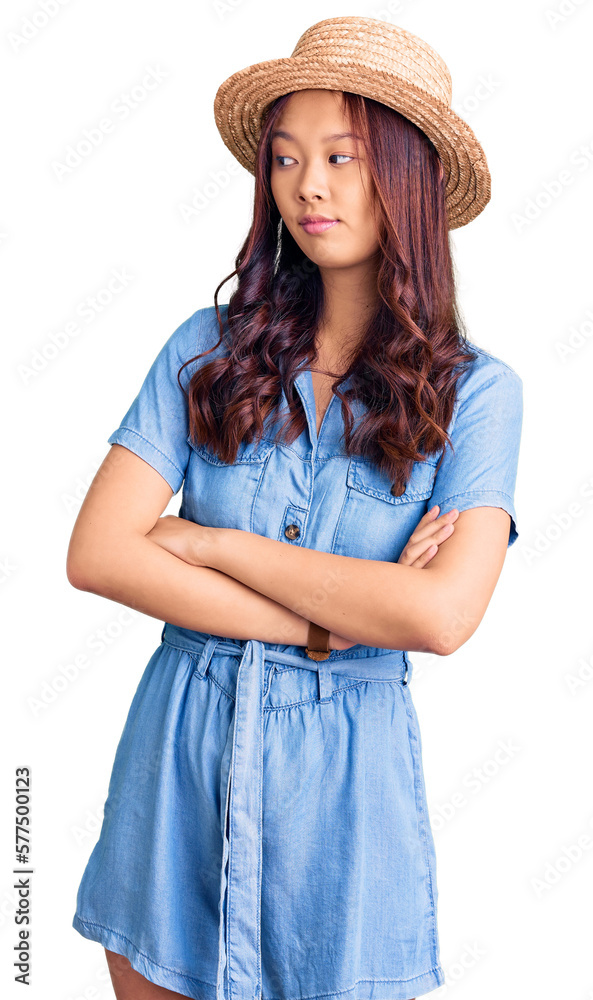 Young beautiful chinese girl wearing summer hat looking to the side with arms crossed convinced and confident Young beautiful chinese girl wearing summer hat looking to the side with arms crossed convinced and confident