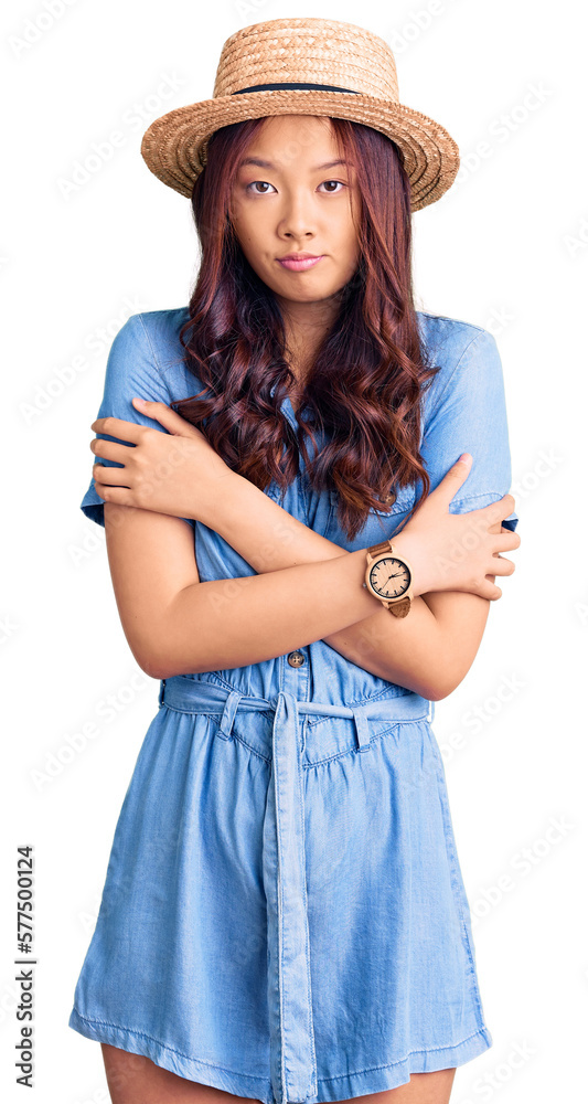 Young beautiful chinese girl wearing summer hat shaking and freezing for winter cold with sad and shock expression on face Young beautiful chinese girl wearing summer hat shaking and freezing for winter cold with sad and shock expression on face
