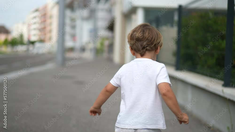 Back of happy kid walking outside in city street. Child standing in urban sidewalk Back of happy kid walking outside in city street. Child standing in urban sidewalk