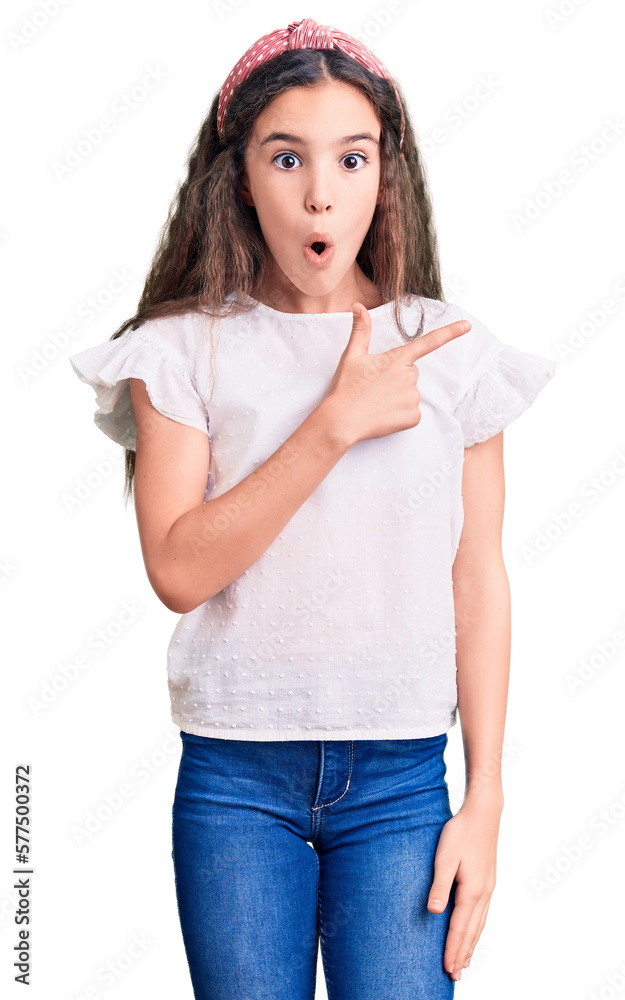 Cute hispanic child girl wearing casual white tshirt surprised pointing with finger to the side, open mouth amazed expression. Cute hispanic child girl wearing casual white tshirt surprised pointing with finger to the side, open mouth amazed expression.