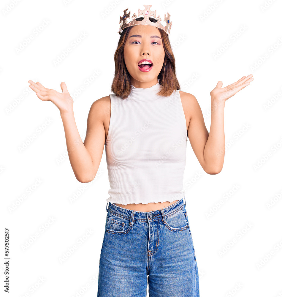 Young beautiful chinese girl wearing princess crown celebrating victory with happy smile and winner expression with raised hands Young beautiful chinese girl wearing princess crown celebrating victory with happy smile and winner expression with raised hands