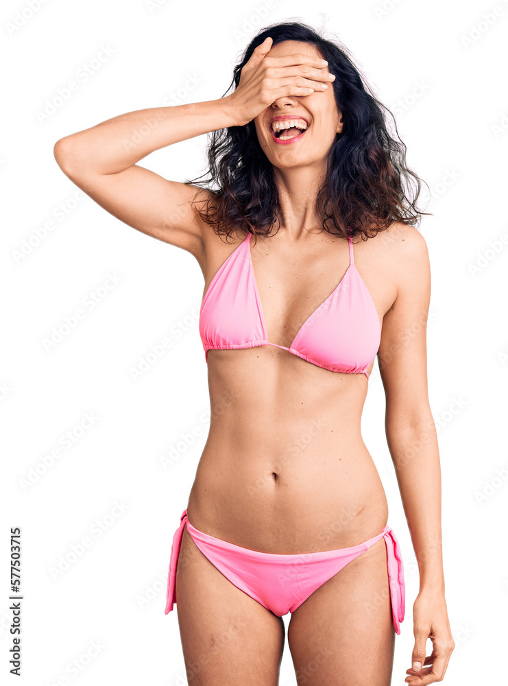Young beautiful hispanic woman wearing bikini smiling and laughing with hand on face covering eyes for surprise. blind concept. Young beautiful hispanic woman wearing bikini smiling and laughing with hand on face covering eyes for surprise. blind concept.