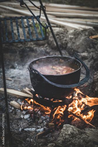 Food in a cauldron on a fire. Cast iron pot with boiling water and vegetable soup. Cooking over an open fire. Off-Grid Cooking Methods without Electricity. Survival and outdoor cooking. Campfire food.